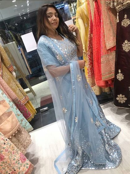 A customer trying on a beautiful powder blue Anarkali gown with intricate silver gota patti work. This piece is perfect for a wedding guest, offering a light and ethereal look.