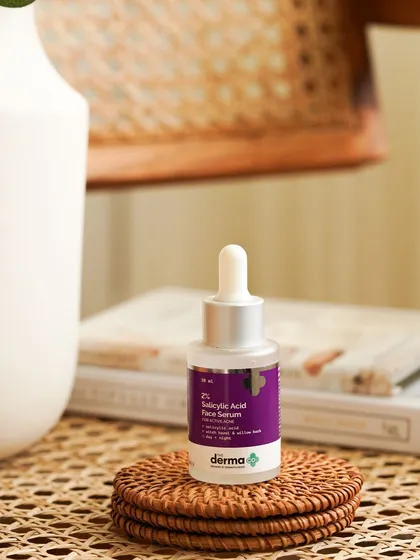 A close-up of the Derma Co. serum on a woven coaster, with soft, natural lighting. This detailed shot emphasizes the product's placement within a calm, aesthetically pleasing daily routine.