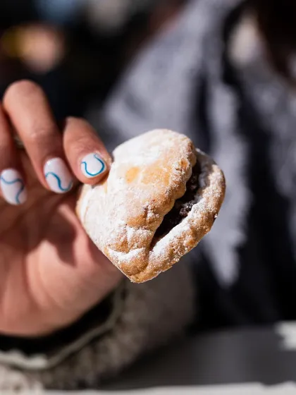 A delicate, powdered sugar-dusted Turkish cookie held in hand. This adds a human element and shows the dainty nature of the pastry.