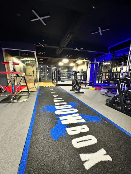 A wide shot of our studio floor, featuring the custom Shadowbox turf track that's perfect for sled pushes, agility drills, and more. In the background, you can see our boxing ring and strength training area.