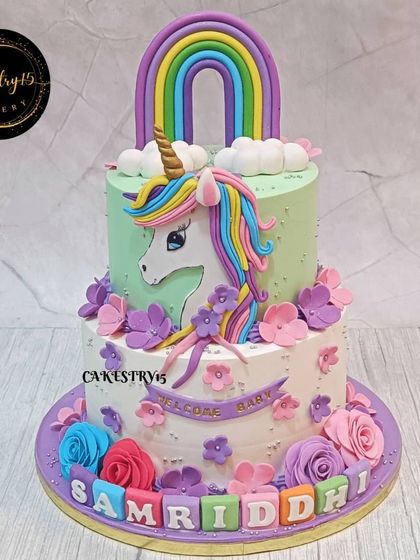 A magical two-tier blueberry unicorn cake designed for a first birthday. This creation features a large fondant unicorn, a colorful rainbow, and floral decorations for a fairytale celebration.