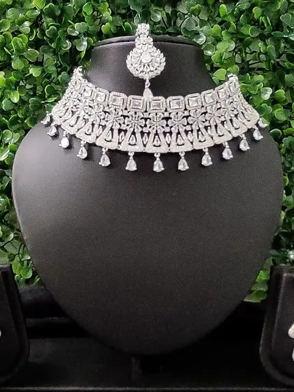 For the modern bride who loves to sparkle, this complete American diamond necklace set is a perfect choice for a reception or cocktail event. It includes a choker, matching earrings, and a delicate maang tikka.