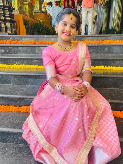 Custom designs aren't just for adults. This adorable client is all smiles in her pretty pink half saree, complete with a delicate net dupatta, designed to be comfortable and beautiful for a family function.