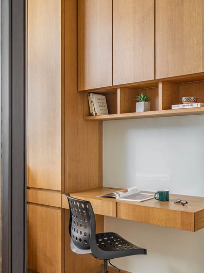 The study area in the guest room features warm brown veneers and is flooded with natural light. A small shelf above the desk provides a perfect spot for books and decorative artifacts.