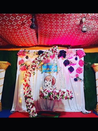 A naming ceremony decoration with a hanging floral cradle and a backdrop of large paper flowers. The setup is simple, elegant, and perfect for home celebrations.