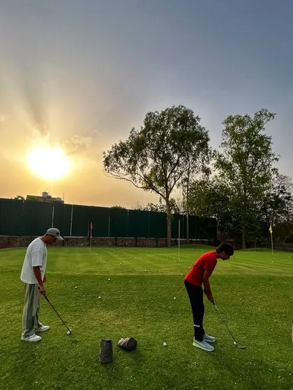 Two golfers practice their putting as the sun sets, casting a golden glow over the green.