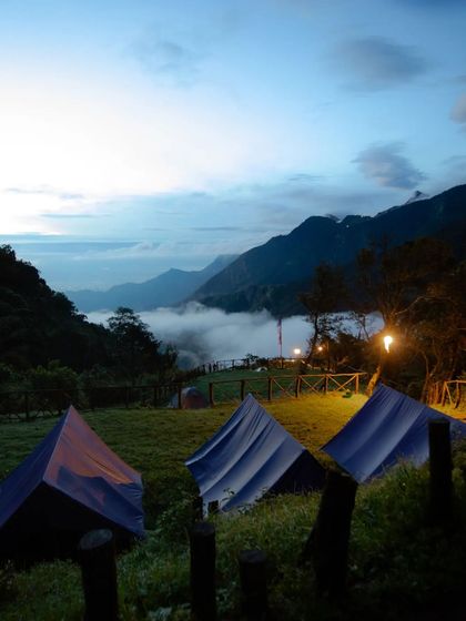 The Munnar campsite at dusk, with tents glowing under the evening sky and a bed of clouds below.