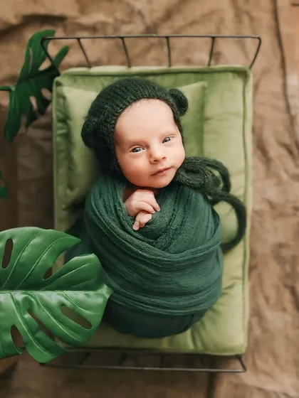 A close-up of this sweet baby, awake and calm in our green-themed setup. The knitted bonnet with little ears adds a touch of whimsy to this safe and comfortable newborn pose.