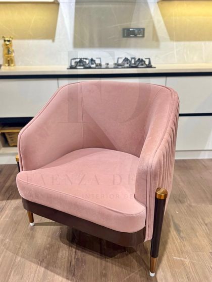 A pair of blush-pink armchairs with pleated backs and tapered legs with brass caps. These chairs are perfect for adding a touch of soft, modern glamour to a living room or kitchen seating area.