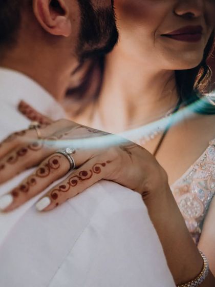 A close-up on the bride's hand resting on the groom's shoulder, showcasing her simple henna and elegant ring.