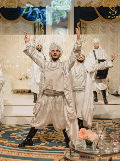 A high-energy performance by dancers in shimmering silver outfits, bringing the celebratory spirit of Bhangra to a regal indoor setting.