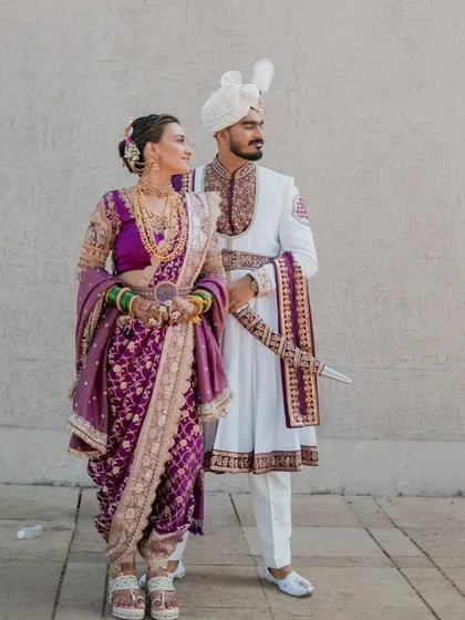 A royal couple look. The bride is in a majestic purple Nauvari, and the groom is in a traditional white sherwani, showcasing my ability to create a cohesive and regal look for both.