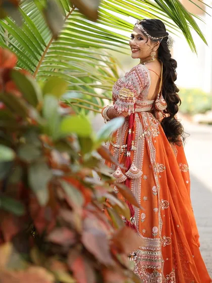 A beautiful shot of the 'Rust Orange Bride', highlighting her long, flowing braid and the intricate details of her lehenga.