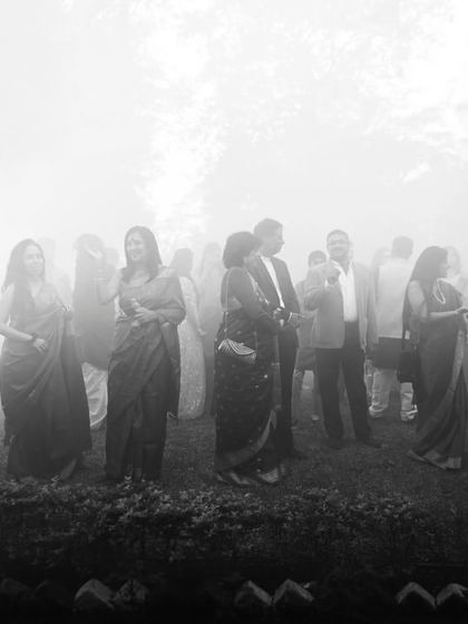 An atmospheric black and white shot of wedding guests mingling in a misty, dreamlike setting. This photo captures the mood and ambiance of the celebration.