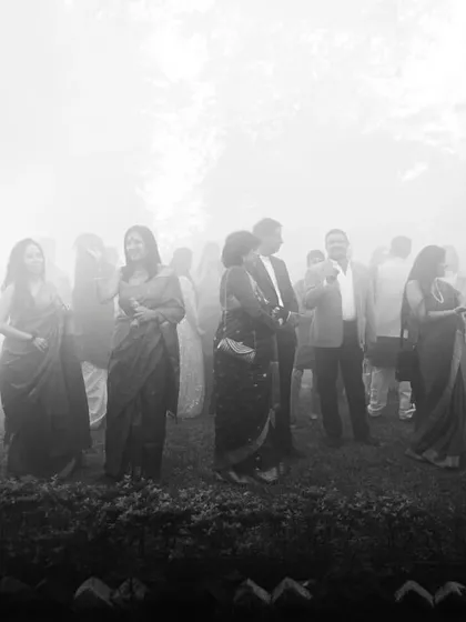 An atmospheric black and white shot of wedding guests mingling in a misty, dreamlike setting. This photo captures the mood and ambiance of the celebration.