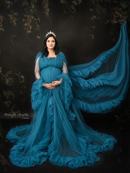 A regal portrait in a deep blue gown. The flowing fabric and the tiara create a majestic look, fit for a queen awaiting her heir.
