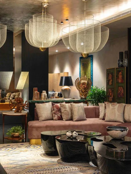A view of the formal living room with its plush pink sofa, black lacquer coffee tables, and large mesh chandeliers. The room is a rich tapestry of textures, from velvet and metal to stone and wood.