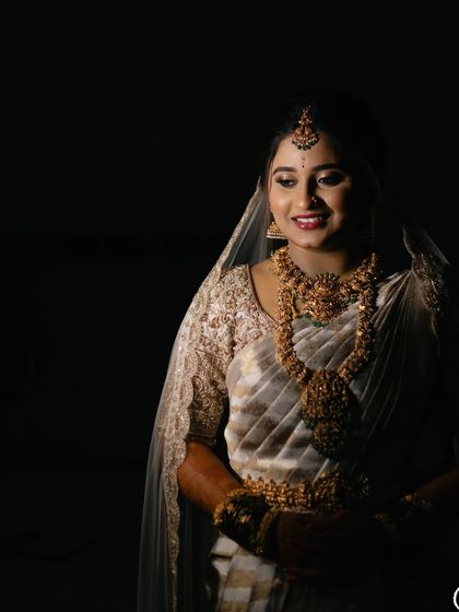 A dramatic portrait of the bride in her white and gold saree, with shadows creating a sense of depth and elegance.