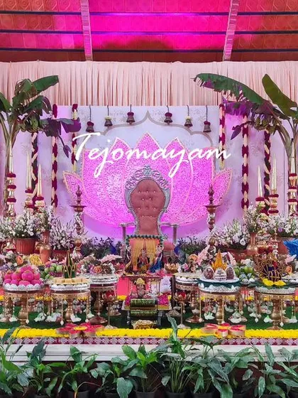A baby shower setup with a lotus-themed backdrop and traditional banana plantains. The arrangement of plates on the red carpeted stage is both grand and auspicious.