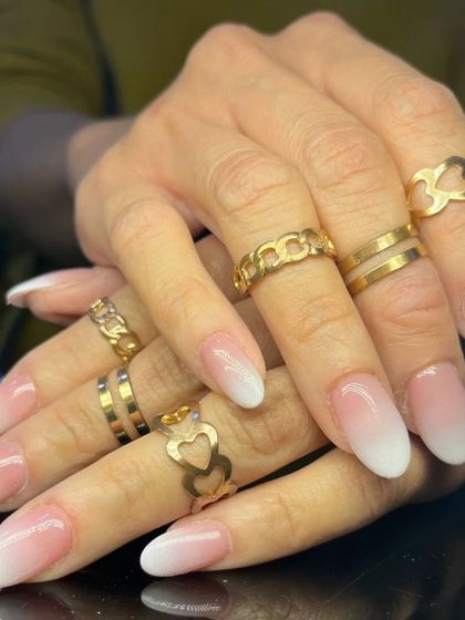 A full set of classic baby boomer ombre nails, styled with elegant gold rings.