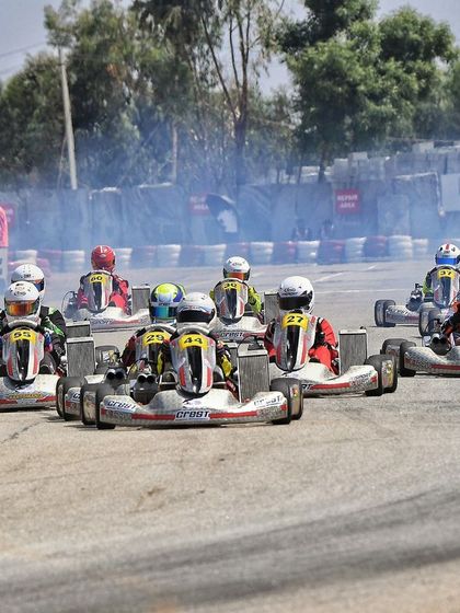 A formation of karts during a practice session, with smoke from the tires indicating the high level of commitment from the drivers.