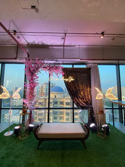 An indoor proposal setup with a stunning city view. We used a pink cherry blossom arch, a "It was always you" neon sign, and glowing butterfly lights to create an unforgettable romantic moment.