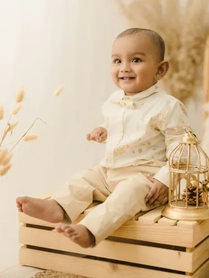 A happy baby boy sits on a wooden crate next to a golden birdcage prop. His bright smile lights up this charming individual portrait.