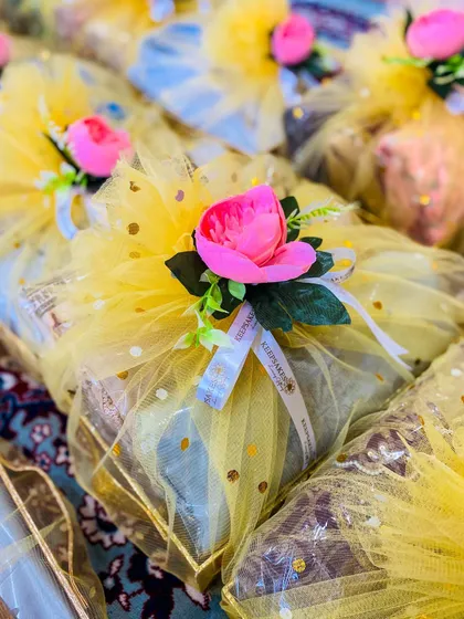 A closer look at the sagan favours, showing the custom 'Keepsakes' ribbon detail. The combination of sunny yellow wrapping and a pink floral accent creates a festive and memorable token of appreciation for wedding guests.