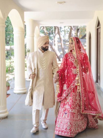 An elegant portrait of a Sikh couple walking hand-in-hand. The classic architecture and their regal attire create a timeless and sophisticated wedding photograph.