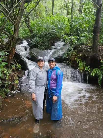 Two trekkers enjoying a stream crossing on the Netravati trail. The path is filled with lush greenery and small waterfalls, especially from June to November.