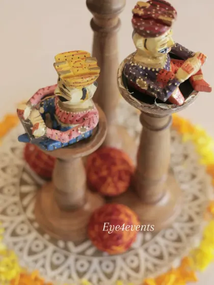 An overhead view of the traditional Rajasthani centerpiece, showing the intricate details of the painted musician figurines and the circular arrangement of marigold petals on a patterned base.