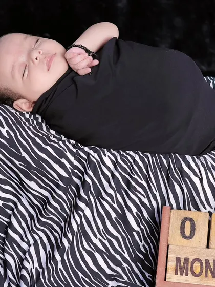 Marking the one-month milestone with a simple and modern setup. The baby is comfortably swaddled on a zebra-print fabric, creating a stylish newborn portrait.