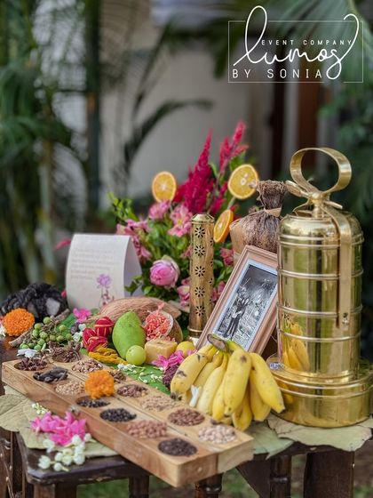 A close-up of the Navadhanyam and other traditional offerings, including a brass tiffin carrier and fresh fruits.
