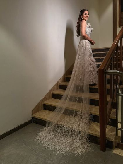 A dramatic shot of the bride on the stairs, her gown's feathered train cascading down. The makeup is equally show-stopping, with a focus on glamour and sophistication.