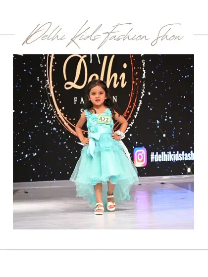 A beautiful high-low dress in aqua blue makes a statement on the runway. The professional lighting and stage setup ensure that every detail of the outfit and the model's performance is captured perfectly.