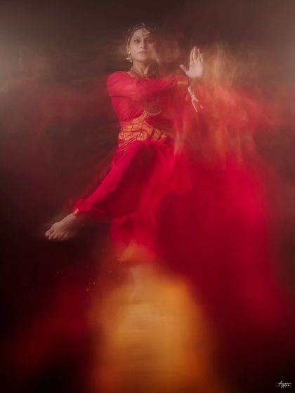 An ethereal and abstract dance portrait. The blur of red and gold light creates a dreamlike quality, with the dancer's form emerging from the haze like a spirit.