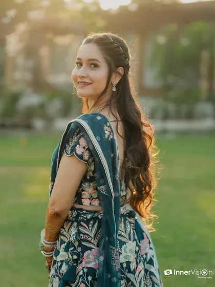 A beautiful outdoor portrait of a bride at her Sangeet. The golden hour sunlight catches her hair, creating a lovely backlight effect as she looks back with a gentle smile.