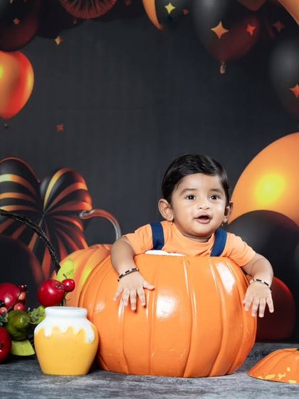 A Halloween-themed shoot with a baby in a pumpkin, surrounded by black and orange balloons.
