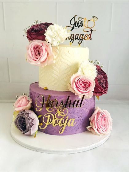 A beautiful two-tier engagement cake with contrasting textures. The top tier is smooth and white, while the bottom features a purple textured design, all brought together with fresh flowers.