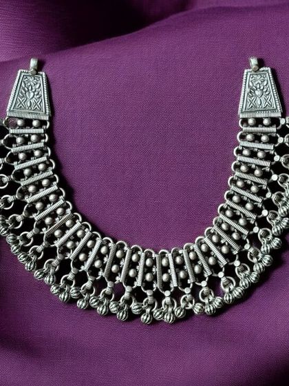 A unique oxidised silver necklace with a choker-like design. The piece is made of multiple linked segments with ghungroo drops.