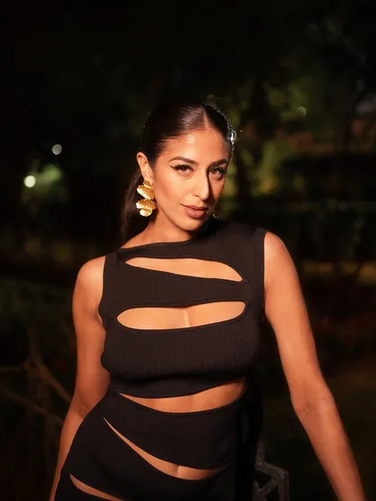 A close-up shot capturing a moment of confidence. The lighting focuses on the model's face and the gold earrings, adding a touch of warmth and luxury to the evening look.