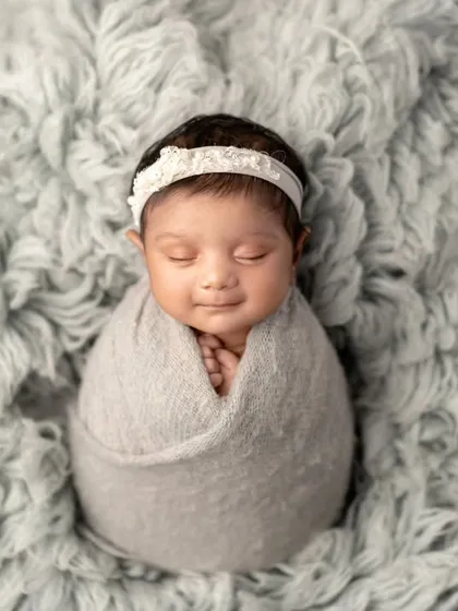 A peaceful smile on a soft bed of grey. This simple, elegant swaddle pose focuses entirely on the baby's serene expression.