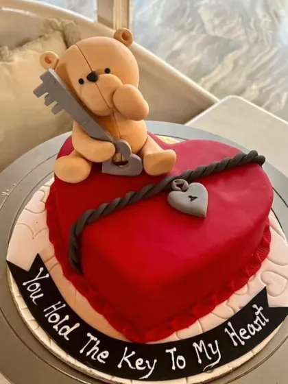 A romantic Valentine's cake with a teddy bear holding the "key to my heart" on a red heart-shaped base.