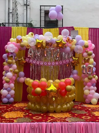An outdoor birthday decoration setup in a tent. I used a combination of pink, yellow, and gold balloons to create a festive stage with a shimmer curtain backdrop.