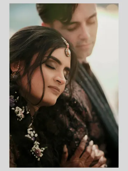 A tender moment where the bride rests her head on the groom's shoulder. The soft lighting and her floral hairpiece add to the romantic feel of this Sangeet portrait.