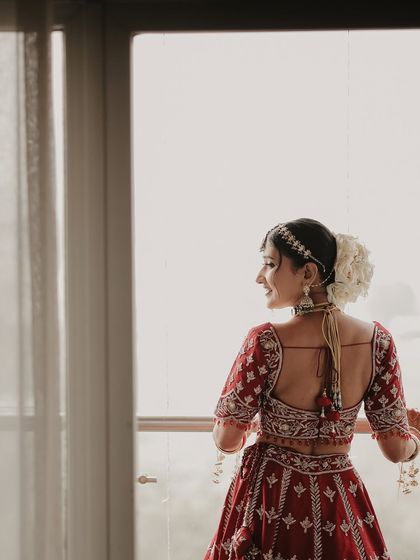 A moment of quiet reflection by the window. This portrait captures the bride looking out, perhaps dreaming of her future, her beautiful hairstyle with white roses adding a touch of elegance.