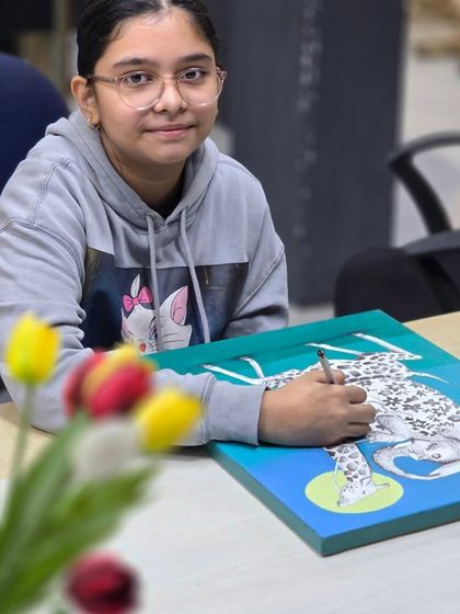 A student works on her drawing at a desk, with tulips in the foreground, adding to the creative atmosphere of our studio.