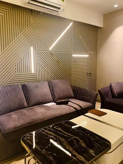 A modern drawing room featuring a custom wall panel with geometric louvers and integrated LED strip lighting. This design element also cleverly conceals a door for a seamless look.