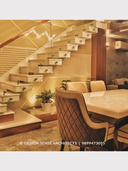 A beautifully lit dining space set against a modern floating staircase. The combination of marble flooring, quilted dining chairs, and architectural lighting creates a truly elegant setting.