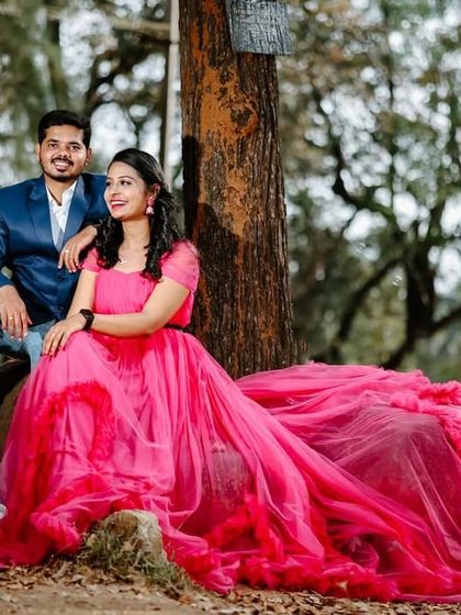 A relaxed and happy pre-wedding portrait in the woods. The long, ruffled train of the magenta gown looks beautiful spread out on the ground.